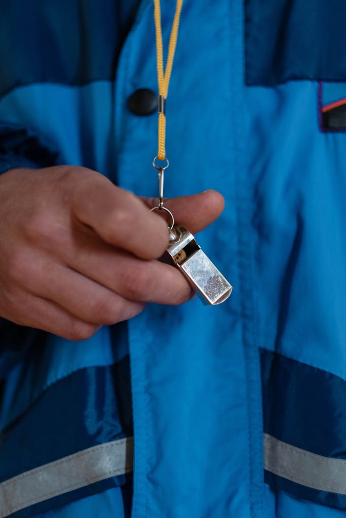 Close-up of a coach's hand holding a whistle, representing sports guidance and teamwork.