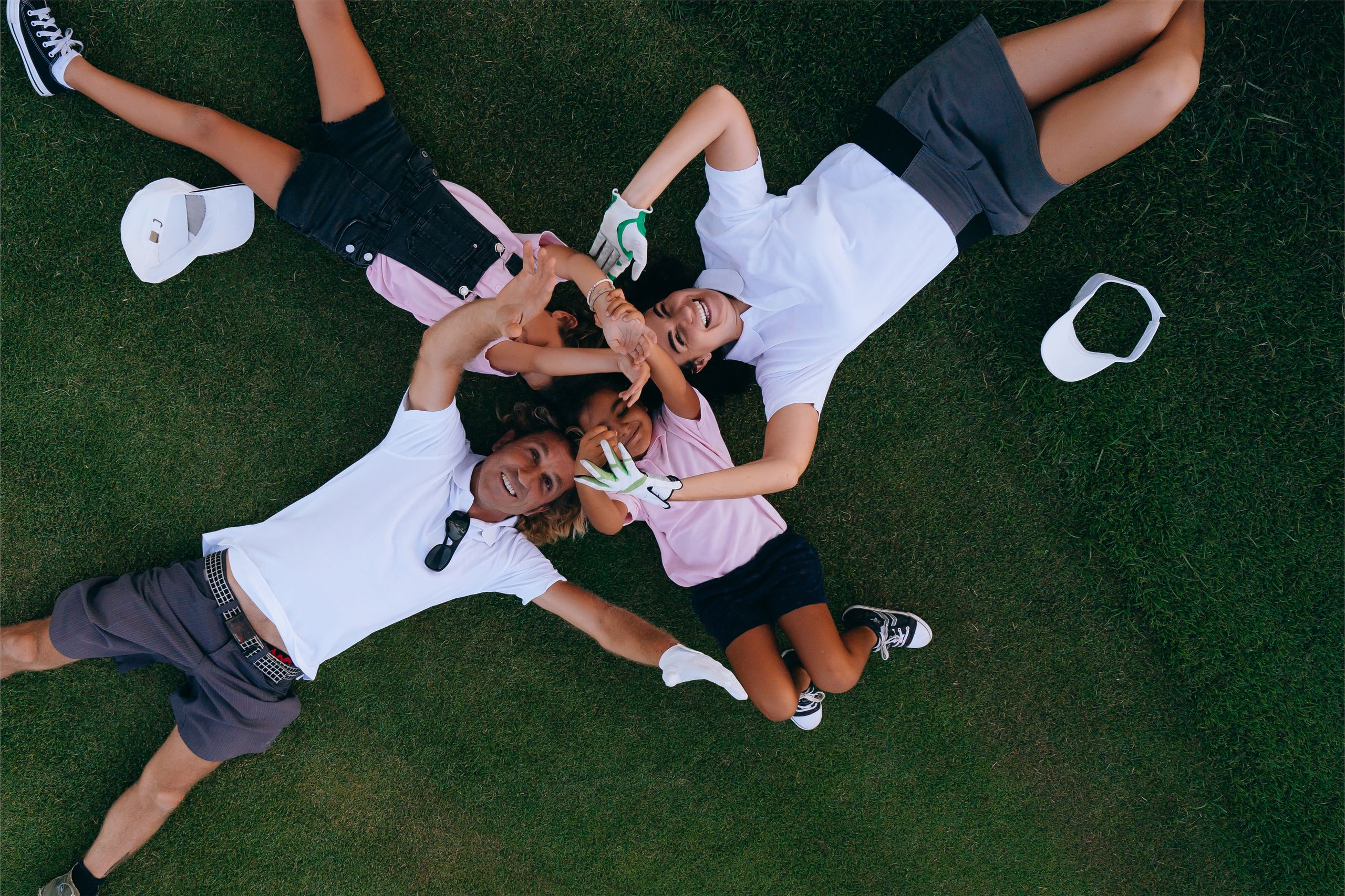 Joyful family in casual attire lying on grass, forming a heart shape with their hands.